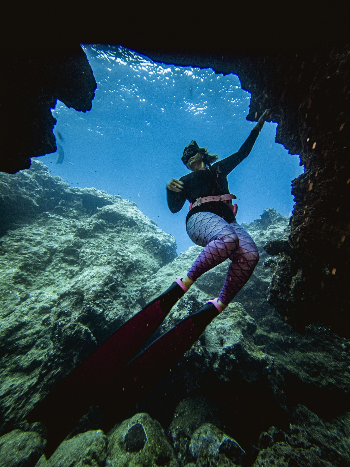 Elaine Hicks moving through a rocky underwater formation while freediving.